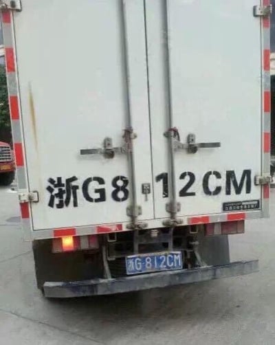 图片展示了一辆白色货车的尾部，车身两侧有红白相间的反光条。货车尾部中央位置用黑色字体写着“浙G8 12CM”，其中“12CM”因间距原因单独成行，下方悬挂的蓝色车牌为“浙G812CM”。整体画面清晰，拍摄场景为室外路面，背景中可见部分其他车辆。

图片的趣味点在于车身文字“浙G8 12CM”的排版巧合，使得“12CM”独立呈现，与车牌形成呼应，可能引发观者的联想和笑意，属于生活中偶然发现的趣味场景。