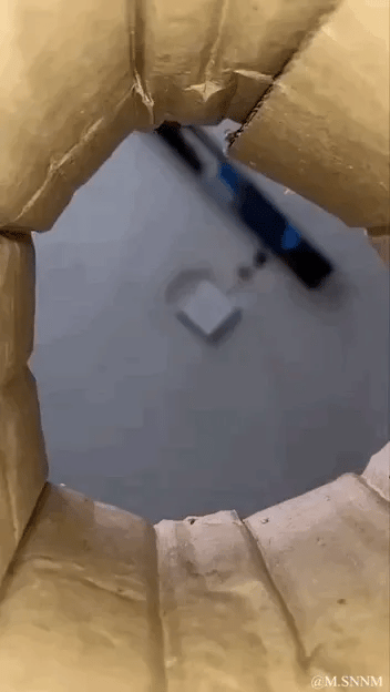 这是一个视觉错位的动态图，透过一个类似纸筒的环形结构看向地面，远处地面上的白色方块因为视角巧合，看起来像是刚好卡在纸筒的孔洞中，营造出一种方块就在孔洞里的错觉，实际二者距离很远，没有双关、谐音梗或暗示内容。