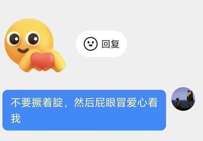 这是一张产生搞笑误解的聊天截图，浅灰色背景左上角是一个3D风格的黄色圆脸比心emoji，emoji面带微笑，双手捧着一颗红色爱心；emoji右侧有一个写着“回复”的白色按钮；图片下方是蓝色的微信聊天气泡，里面的文字内容为“不要撅着腚，然后屁眼冒爱心看我”，聊天气泡右侧有一个圆形用户头像，头像里包含两个人物。因为emoji的红心位置刚好在圆脸下方，被调侃看错成撅着屁股，屁眼冒出爱心，因此产生了低俗搞笑的效果，属于网络上流行的视觉误解类搞笑梗。