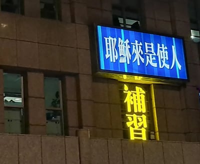图片拍摄于夜晚街头，一块蓝色LED显示屏写着“耶稣来是使人”，下方为黄色发光字“补习”。原意为宗教宣传标语“耶稣来是使人……”（未完），但和“补习”的招牌组合起来，意外形成了谐音与双关效果，让人误以为在宣传耶稣来补习，有种荒诞的幽默感。

**双关梗说明**：宗教标语与补习班牌子的拼贴，营造出“耶稣也来补习”的错觉。通常在线上被调侃为神奇招牌、错误分割、误导宣传的典型梗图。易于二创、恶搞。
