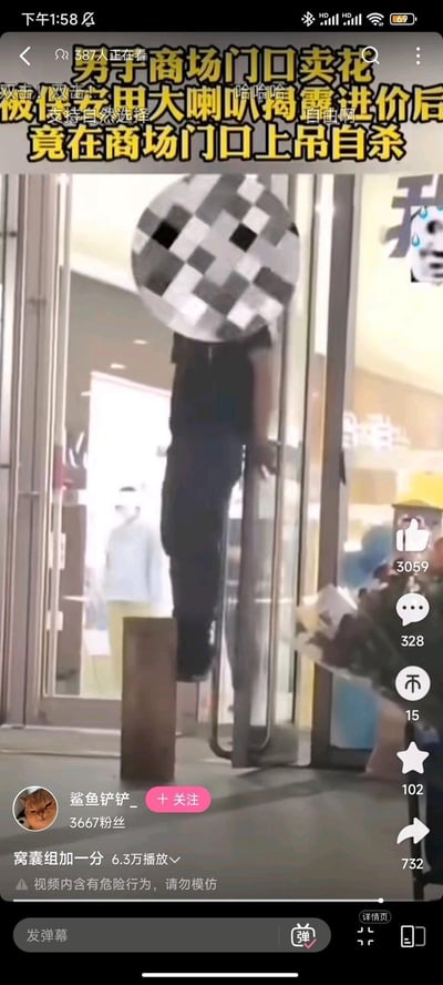 这是抖音平台的一段摆拍整活视频截图，画面中一名男子借助商场玻璃门的把手和下方的柱子，摆出上吊的姿势，头部被打码遮挡。视频配用博眼球的虚假标题“男子商场门口卖花 被保安用大喇叭揭露进价后 竟在商场门口上吊自杀”，实际是恶搞摆拍，视频下方标注“窝囊组加一分”，并附带“视频内含有危险行为，请勿模仿”的提示，弹幕里有“支持自然选择”“哈哈哈”等调侃内容，视频作者为抖音用户“鲨鱼铲铲_”，已有6.3万播放量。