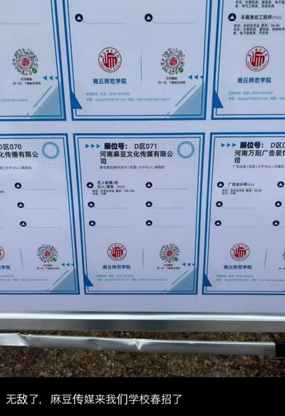 这是商丘师范学院春季招聘会的现场实拍图，画面展示了多个企业的招聘展位信息，其中位于D区071的河南麻豆文化传媒有限公司展位格外引人关注：该公司主营影视策划、制作、发行，为民营少于50人的企业，招聘艺人助理/经纪人/星探50人，要求中专及以上学历，薪资15k-25k，专业不限。由于“麻豆”一词与知名成人内容品牌“麻豆传媒”同名，引发该校学生的调侃，图片下方配文“无敌了，麻豆传媒来我们学校春招了”。同时画面中还展示了车载测试工程师、广告设计师等其他岗位的招聘信息，以及商丘师范学院的联系电话、邮箱、网址等校招相关联系方式。