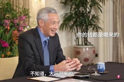 这是一张对新加坡前总理李显龙的公开采访截图进行文字加注改编的梗图，图中上方配文「你的钱都是哪来的」，下方配文「不知道，大风刮来的」，用正式严肃的采访场景搭配戏谑的回答文字，形成强烈反差，制造搞笑效果，用来调侃被问及收入来源时的敷衍回应，图中没有双关、谐音梗等内容。