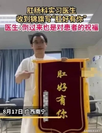 这是一张视频截图，画面主体是一位身处医院室内环境的肛肠科实习医生，他身着白色工作服，面带微笑，双手举着一面红底黄字的锦旗，并用手指向锦旗上的文字。锦旗上写着“肛好有你”，这是“刚好有你”的谐音梗，既贴合肛肠科的科室属性，又巧妙表达了患者对医生的感谢。图中的文字标注显示，该事件发生在8月17日的广西南宁，医生表示这句话倒过来“你有好肛”也是对患者的健康祝福，形成了医患之间温暖的双向致意。背景中可以看到医院的蓝色窗帘和办公桌椅，右下角带有“GAMERSKY”的水印。