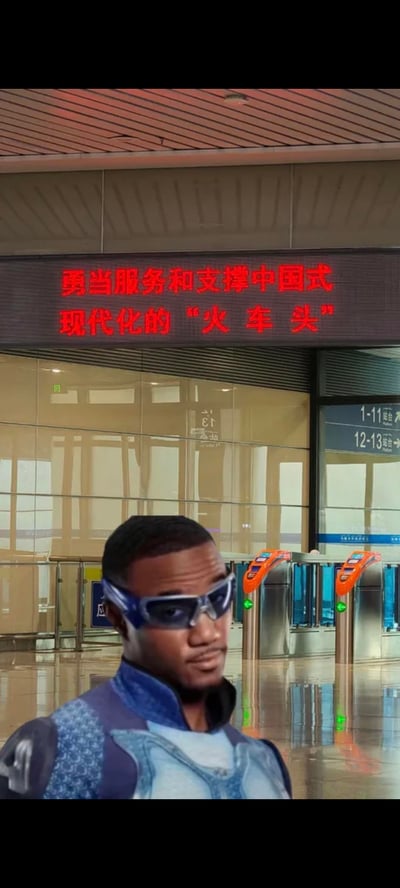 图片展示了一个穿着蓝色未来风格服装、戴着蓝色护目镜的非裔男性角色站在火车站大厅内。背景中可以看到玻璃幕墙、自动检票闸机和显示站台信息的屏幕。最上方有一个大型电子显示屏，滚动显示红色文字："勇当服务和支撑中国式现代化的'火车头'"。整个场景看起来像是将科幻电影中的角色合成到了现实的中国火车站环境中，形成了一种现实与虚构的有趣对比。