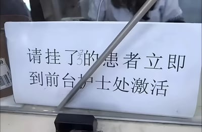 图片中展示了一块医院的指示牌，上面用黑色字体写着："请挂了号的患者立即到前台护士处激活"。指示牌为白色背景，放置在医院的某个服务台区域，背景中隐约可见工作人员。
