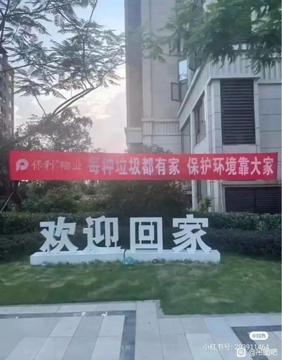 这是保利物业管辖小区的实拍场景，草坪上设置着白色立体字“欢迎回家”，其上方悬挂着保利物业的红色垃圾分类宣传横幅“每种垃圾都有家 保护环境靠大家”。两个标语的位置组合形成了趣味巧合，让“欢迎回家”仿佛是对“垃圾”的欢迎，产生了搞笑的反差效果。
