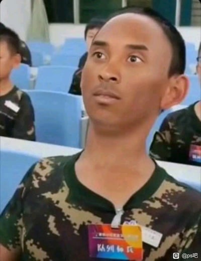 图片中一名身穿迷彩服的男子坐在蓝色座椅的礼堂中，头部微微后仰，双眼凝视上方，表情严肃专注。背景中可以看到其他穿着类似服装的人也坐在座位上，整体场景像是在参加某种集体活动或会议。