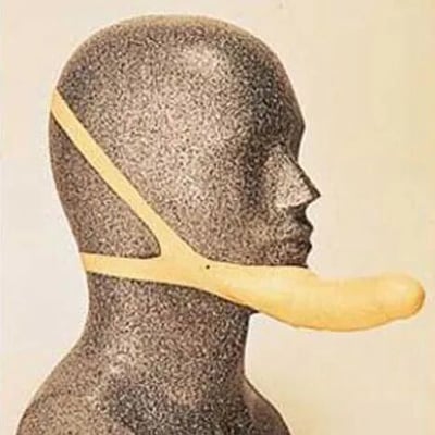 图片中展示了一个灰色的人体模型头部，模型佩戴着一个造型奇特的米色装置。该装置由一条带子从头部后方延伸，在下巴处连接着一个长条形的弯曲部件，整体看起来像是某种面部或下巴的辅助器具。背景为简单的浅色，没有其他装饰或文字。