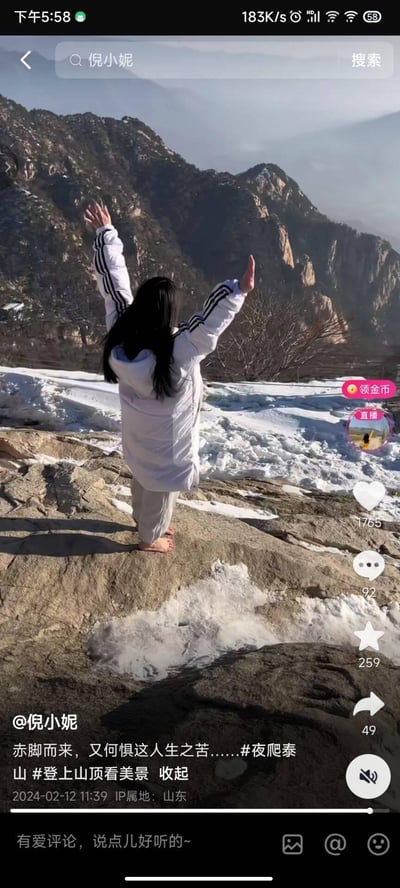 这是一张抖音短视频截图，画面中博主倪小妮背对着镜头，赤脚站在留有残雪的泰山山顶岩石上，双臂高高举起，背景是巍峨陡峭的泰山山峦，冬日的残雪点缀在岩石间，氛围开阔清冷。配文“赤脚而来，又何惧这人生之苦……”传递出直面困难、豁达励志的人生态度，带有#夜爬泰山 #登上山顶看美景的话题标签。