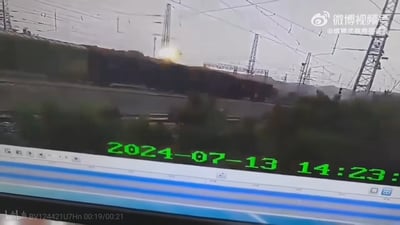 这是一张监控设备的屏幕截图，画面显示2024年7月13日14:23左右，一处铁路线路区域内的货运列车出现异常状况，车厢位置可见明显火光，背景是铁路的接触网铁塔群，画面带有运动模糊效果，推测是列车在行驶过程中发生了起火或脱轨类的突发事故，整体场景氛围紧张。