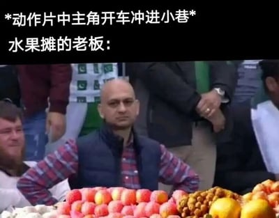 图片上方配有文字'*动作片中主角开车冲进小巷*'和'水果摊的老板：'，下方是一张真人照片：一位穿着格子衬衫和深色马甲的男子双手叉腰站在水果摊后，摊位上摆满了苹果、草莓、橙子等水果。男子表情淡定，与动作片中紧张刺激的场景形成幽默反差，调侃了电影中常见的夸张情节与现实中普通人反应的对比。