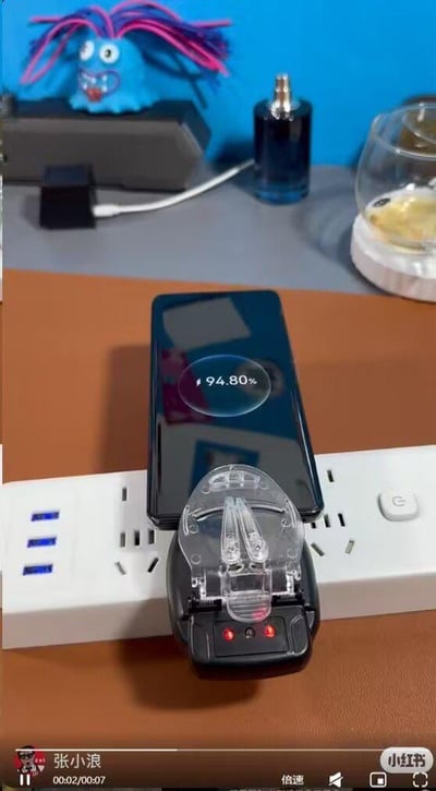 这是一张竖屏的视频截图，展示了一个极具创意的应急充电方法：将老式万能充的充电夹夹在智能手机的中框触点位置，随后把万能充插在多口插线板上，手机屏幕亮起并显示当前电量为94.80%，呈现出正在充电的状态。画面背景中可见蓝色桌面摆件、香水瓶、带容器的小物件以及带有USB接口的白色插线板。截图底部显示这是小红书用户“张小浪”发布的7秒短视频的第2秒画面，带有小红书平台的标识和视频播放控件。这个方法利用万能充的通用充电特性，实现无充电线时给手机应急充电，属于生活实用小技巧类内容。