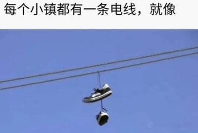 图片上方有一行文字“每个小镇都有一条电线，就像”，下方是一张照片，展示了一双黑色的鞋子被挂在两根平行的电线上，背景是纯净的蓝色天空。这张图通过日常生活中常见的“电线挂鞋”现象，引发人们对小镇共同记忆和标志性场景的联想，带有淡淡的怀旧情绪和对平凡生活细节的观察。