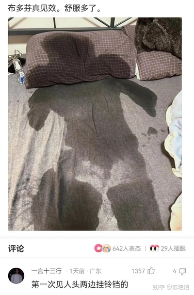这是一张生活场景梗图，床上的大片汗渍形成了酷似人形的视觉效果，看起来如同一个人躺在床上的影子。图上方配文“布多芬真见效。舒服多了”，这里的“布多芬”是退烧药“布洛芬”的谐音，暗示是发烧出汗后退烧的状态。评论区高赞评论“第一次见人头两边挂铃铛的”则调侃了汗渍的形状，将汗渍的边缘戏称为人头两侧的铃铛，利用视觉错位和谐音梗制造出轻松搞笑的效果，生动表现了退烧后身体排出大量汗水的真实又滑稽的场景。