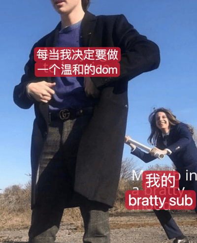 图片展示了两个年轻人的户外场景。前景中一人穿着黑色大衣和紫色T恤，双手整理外套，表情严肃。背景中另一人穿着深色西装，手持卷纸筒，面带笑容，摆出即将从背后击打的姿势。图片上方有红色文字覆盖："每当我决定要做一个温和的dom"，右下角有红色文字："我的bratty sub"。通过前后人物的动作对比和文字内容，形成了一种反差幽默，表现了想做温和主导者却遇到调皮服从者的无奈场景。