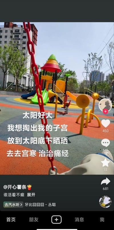 这是一张抖音平台的短视频截图，背景是阳光充足的户外儿童游乐场，色彩鲜艳的滑梯、传声筒等游乐设施分布在彩色地面上，前景是秋千的红色链条，右下角露出拍摄者的部分腿部。图中用夸张荒诞的文字吐槽：“太阳好大 我想掏出我的子宫 放到太阳底下晒晒 去去宫寒 治治痛经”，以这种极端的玩笑方式抒发被宫寒、痛经困扰的无奈，精准戳中不少女性的生理痛点，风格接地气又充满搞笑自嘲的情绪，没有双关、谐音梗等特殊修辞，纯靠夸张表达引发共鸣。
