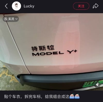 这是一张社交平台发布内容的截图，画面主体为一辆新能源汽车的车尾部位，原本的特斯拉MODEL Y车标在车主贴车衣拆卸后，被工作人员错误拼接，汉字部分变成了“持斯牝”，字母部分在MODEL Y后面多加了一个+号，变为“MODEL Y+”。截图底部是发布者的配文，附带两个流泪的表情，体现出发布者无奈又好笑的情绪。截图顶部可见发布者用户名、平台的关注、返回、分享按钮以及实况标识，右下角露出部分绿色新能源汽车车牌。