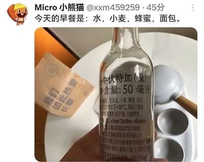社交媒体用户"Micro 小熊猫"发布的一条图文动态，配文称"今天的早餐是：水，小麦，蜂蜜，面包。"，下方配图为一只手拿着一瓶50毫升装的"小牛伏特加（绿）"，瓶身标签显示其配料正是水、小麦、蜂蜜、面包。通过将伏特加的配料表一本正经地描述为"早餐"，形成幽默调侃的效果，属于生活类玩梗内容。