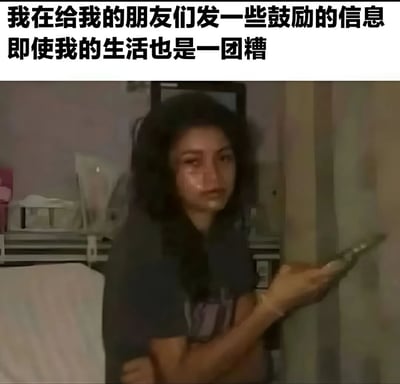图片上方有两行黑色文字：'我在给我的朋友们发一些鼓励的信息 即使我的生活也是一团糟'。下方是一张室内照片，一名长发女性穿着深色上衣，手持手机，表情略显疲惫，背景中可见一些生活用品，整体环境略显凌乱。图片通过文字与人物状态的对比，展现了在自身生活不顺时仍努力鼓励朋友的矛盾与温暖。