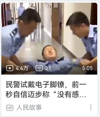 这是一段来自哔哩哔哩平台的视频截图，画面中三名身着警服的人员在走廊里，中间的民警被左右两名同事架着，仰头张嘴，面部露出痛苦的神情。下方的视频标题显示“民警试戴电子脚镣，前一秒自信迈步称‘没有感...”，结合标题可以推测，这名民警原本自信地试戴电子脚铐，声称没有感觉，结果脚铐触发了限制功能，让他瞬间失去行动能力，形成了强烈的前后反差，制造出搞笑的效果。图中没有双关、谐音梗或暗示内容。