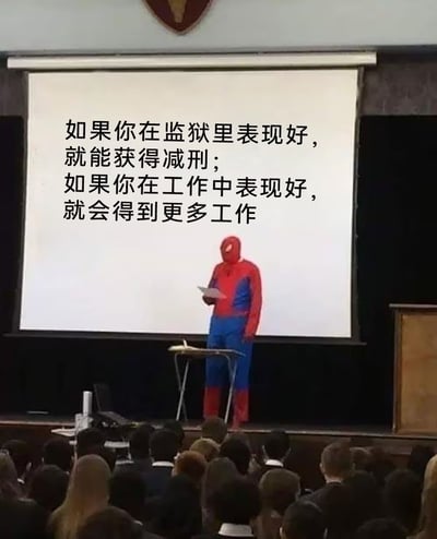 这张图是一位穿着蜘蛛侠服装的人站在讲台前，面对观众做演讲。投影布上显示着一段文字，通过对比监狱和职场表现好的不同后果，表达了对职场剥削现象的讽刺和调侃。

图片用蜘蛛侠“正经讲道理”的反差感制造了幽默氛围，且具有明显的社会讽刺意味。

有明显的反差梗和双关，暗示职场努力并不一定带来激励，反而带来更多工作量，形成幽默和荒诞感。