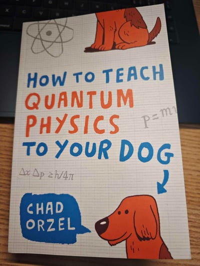 这是科普读物《How to Teach Quantum Physics to Your Dog》（《给你的狗狗讲量子物理》）的官方封面，背景采用方格笔记本纸的样式，搭配两只卡通狗狗形象，同时印有原子结构示意图、动量公式p=mv（部分显示）、不确定性原理公式ΔxΔp≥h/4π这些量子物理相关的符号与公式。书籍以给狗狗讲解量子物理的幽默设定，将原本高深晦涩的量子物理知识包装得通俗易懂，充满趣味性，旨在降低科普门槛，让更多人能接触量子物理知识。