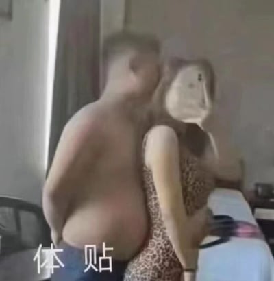 图片中展示了一对情侣的亲密瞬间，男子赤裸上身从后方环抱着身穿豹纹连衣裙的女子，女子侧身转头，手中似乎拿着物品。画面下方有“体贴”二字，可能是对这一场景的描述或标题。