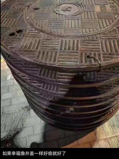 这张图利用视觉错位效果，让地面上的单个圆形井盖看起来如同堆叠起来的多层，营造出井盖仿佛很轻易就能取走的错觉。图片下方配文“如果幸福像井盖一样好偷就好了”，用这种生活化的调侃方式，表达了人们对幸福的向往，同时也暗含幸福难以追寻、获得不易的无奈情绪，通过日常物品的视觉梗搭配扎心文案，形成反差感，引发共鸣。