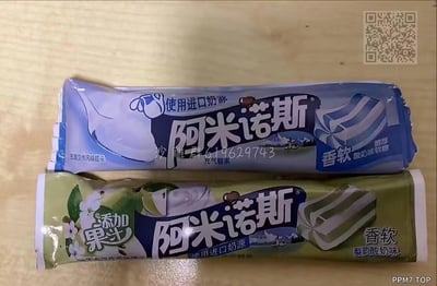 图片实拍展示了两款阿米诺斯品牌的充气软糖，上方为蓝色包装的酸奶味软糖，标注使用进口奶源，主打香软口感；下方为绿色包装的梨韵酸奶味软糖，标注添加果汁，同样主打香软口感。两款包装风格模仿知名糖果品牌，属于山寨食品，图中还带有QQ群号和网站水印，推测是网友在社群中分享的实拍图。