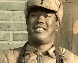 这是一张出自国产抗战剧《亮剑》的动态GIF图，图中角色王有胜身着土黄色旧军装、戴着军帽，露出一口白牙，一脸憨厚又得意地傻笑着。这个画面常被网友用作表情包，用来传递开心、得意甚至幸灾乐祸的情绪，是网络上流传度很高的表情素材。
