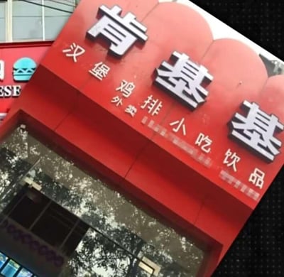 这是一张实拍的街边山寨快餐店招牌照片，招牌以红色为底色，最上方是三个醒目的白色立体大字“肯基基”，明显模仿知名快餐品牌“肯德基”的命名方式，属于谐音山寨。下方用白色小字标注了店铺的经营品类：汉堡、鸡排、小吃、饮品，还附带“外卖”字样。照片左侧能看到隔壁店铺的部分招牌，整体是典型的街边小店的招牌样式，这类山寨店铺通常通过模仿知名品牌的名称来吸引顾客，容易让人联想到肯德基，产生调侃的趣味。