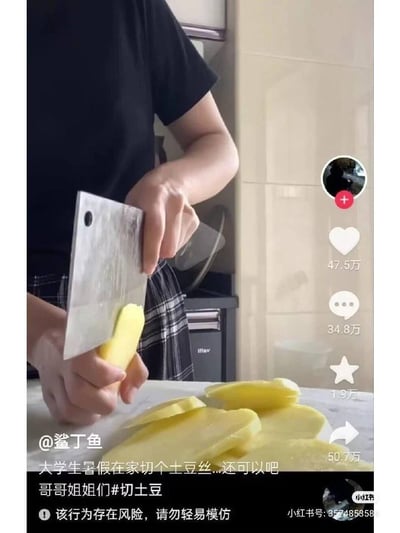 这是一张小红书视频截图，画面中一名大学生正用危险的方式切土豆：直接用手按着土豆贴在菜刀上切片，案板上已经有切好的数片土豆。配文写道“大学生暑假在家切个土豆丝...还可以吧 哥哥姐姐们#切土豆”，同时平台标注了“该行为存在风险，请勿轻易模仿”的提示。画面右侧显示该内容在小红书的互动数据：点赞47.5万、评论34.8万、收藏1.9万、转发50.7万。
没有双关、谐音梗或暗示内容。