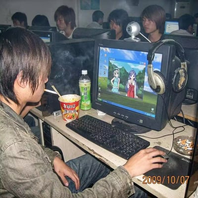 2009年10月7日的网吧场景，画面中心是一位留着长发的少年，他嘴里叼着烟，正用筷子吃着康师傅红烧牛肉面，同时注视着电脑屏幕。屏幕上显示着两个动漫少女角色的画面，旁边放着一瓶绿茶饮料和一副老旧的耳机。周围还有其他年轻人在使用电脑，整个网吧环境略显昏暗，空气中弥漫着烟雾，展现了21世纪初中国网吧的典型样貌。
