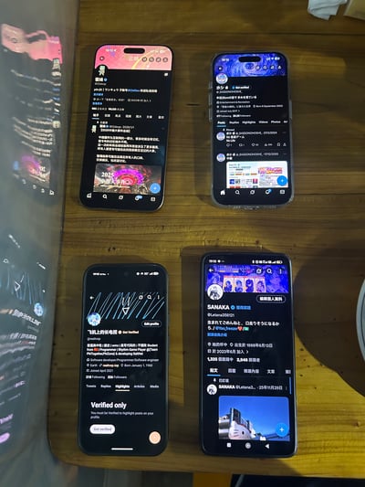 图片展示四部智能手机并排摆放在木质桌面上，屏幕均显示X（原Twitter）平台的界面内容。手机屏幕分别展示了不同用户的资料页、帖子动态等，包含用户名（如'SANAKA921'、'飞机上的长颈鹿'）、加入日期（如'Joined September 2009'）、帖子数量（'1355 帖子'）、关注者数（'2.946 追随者'）及个人简介（如'Student, Software engineer'）等信息。整体场景为日常桌面环境，光线自然，构图清晰，主要突出多设备同时展示社交媒体平台内容的状态。