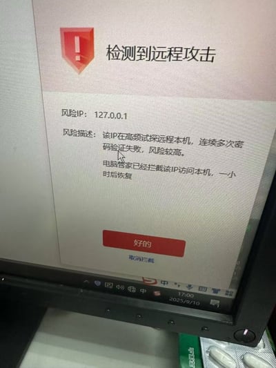 电脑屏幕显示安全警报窗口，标题为“检测到远程攻击”，显示风险IP为127.0.0.1（本机回环地址），提示该IP在高频试探远程本机并多次密码验证失败，已被电脑管家拦截一小时。窗口下方有“好的”和“取消拦截”按钮。屏幕底部显示系统时间为2025年9月10日17:00，任务栏有音量、网络等图标。显示器下方可见绿色包装的药片和铝箔包装的药片。

图片存在明显的技术梗：127.0.0.1是本机回环地址，代表电脑自身，所谓“远程攻击”实际上是电脑自己攻击自己，形成荒诞幽默的效果。