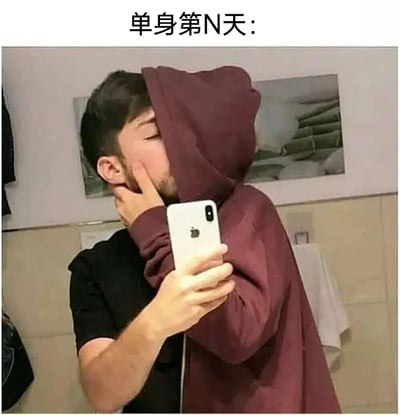 图片展示了一位穿着酒红色连帽衫的男子在浴室自拍的场景。他将连帽衫的帽子拉起盖住头部，左手拿着白色iPhone手机自拍，右手则放在脸颊上模拟亲吻的动作，表情陶醉。图片上方配有文字"单身第N天:"，通过夸张的自我安慰行为幽默地表现了单身人士的生活状态，带有自嘲和搞笑的意味。