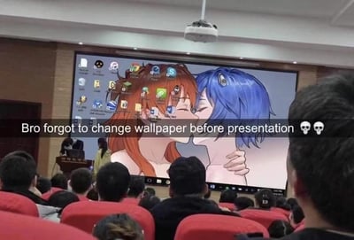 这是一张在大学阶梯教室拍摄的照片，展示了一个社死现场：演讲者在进行演示时，大屏幕上意外显示了他未更换的动漫壁纸，壁纸上是两个动漫人物（一个红发一个蓝发）正在亲密接吻。教室里坐满了观众，大家都在注视着这个尴尬的场面。图片上方有文字"Bro forgot to change wallpaper before presentation 💀💀"，生动描述了演讲者忘记更换壁纸的失误。