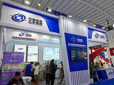 这是在中国-南亚博览会上的中国兵器工业集团旗下北方夜视科技研究院集团有限公司的展台，展台采用蓝白为主的现代科技风格设计，展示了iEye系列手持防爆气体检测仪、PARES 2000大气污染气体红外监测系统等光学检测设备，同时设有云南老字号“云光熊猫望远镜”的追光研学项目宣传区。现场有不少观众正在体验光学观测设备，氛围热闹，呈现出专业的科技展会产品展示与互动场景。