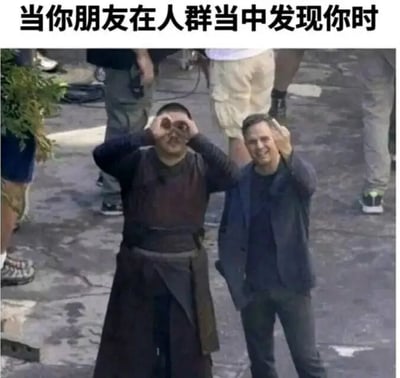 图片上方有文字‘当你朋友在人群当中发现你时’，下方是一张现场照片，左侧男子双手做望远镜状兴奋地望向远方，右侧男子微笑着挥手致意，背景中有工作人员，整体营造出朋友在人群中发现彼此的开心场景。