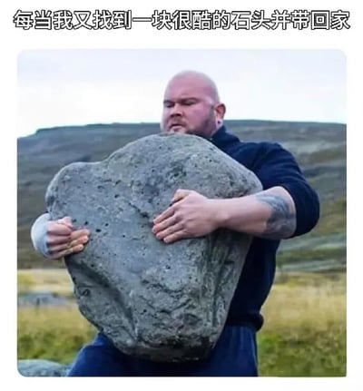 图片展示了一位肌肉发达的光头男性在户外吃力地搬运一块巨大的石头，他表情严肃，双臂紧紧抱住石头，背景是开阔的山野。图片上方配有文字“每当我又找到一块很酷的石头并带回家”，通过强壮男性搬运巨石的夸张场景，幽默地表现了人们找到心仪石头时即使沉重也要带回家的执着心态。