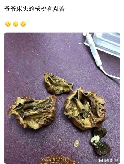 这是一个生活乌龙类梗图：图中展示了被掰开的“核桃”，但实际上这是老人用来盘玩的文玩核桃，并非食用核桃，其内部已经干枯变质。配文“爷爷床头的核桃有点苦”，讲述了拍摄者误将爷爷的文玩核桃当成食用核桃吃下，发现味道发苦才意识到搞错了的趣事。笑点源于混淆了文玩与食用核桃的用途，产生的搞笑误会。