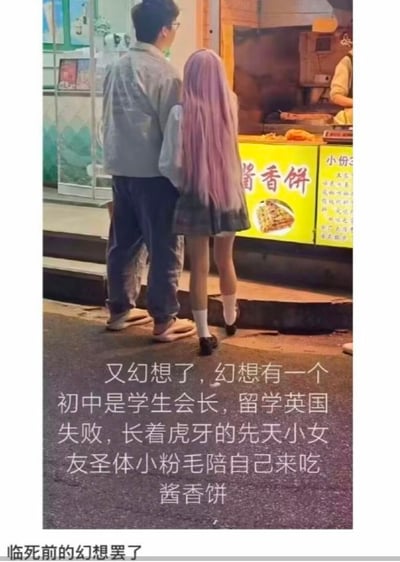 夜晚街边，一名戴眼镜的男子与一位留着粉色长发的女孩并肩站在酱香饼摊位前，一同等待美食。图片下方配有文字，描述了一段充满细节的幻想：希望有一个初中曾任学生会会长、留学英国失败、长着虎牙的「先天小女友圣体小粉毛」陪伴自己吃酱香饼，最后以「临死前的幻想罢了」收尾，用自嘲的语气表达了对理想伴侣和简单幸福的向往与无奈。