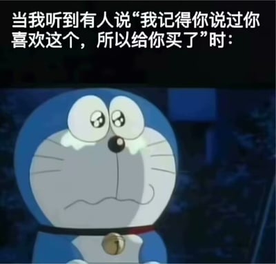经典动画角色哆啦A梦的表情包，上方配有文字“当我听到有人说‘我记得你说过你喜欢这个，所以给你买了’时：”。画面中哆啦A梦瞪大双眼，瞳孔放大，脸颊略带红晕，表情既惊讶又有些不知所措，生动展现了收到他人用心记住自己喜好并赠送礼物时的复杂情绪，既有被重视的感动，又有一时语塞的呆萌反应。