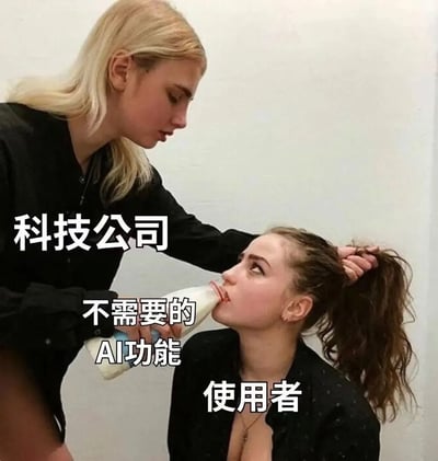 这是一张经过文字标注改编的搞笑梗图，画面中共两名女性：站着的金发女性身上标注「科技公司」，她一手拽住坐着的棕发女性的头发，一手将奶瓶塞进对方口中，奶瓶旁标注「不需要的AI功能」，被迫仰头喝奶的棕发女性身上标注「使用者」，她面露不情愿、翻白眼的神态十分生动。该图用来讽刺当下科技行业的乱象：很多科技企业不顾用户真实需求，在各类产品中强行塞入大量用户并不需要的AI相关功能，强迫用户接受使用，引发了广大用户的共鸣。