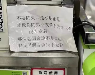 图片展示了一张贴在金属机器（疑似收银或自助服务设备）上的白色标语，内容为：“不要问东西是不是正品 就像你问男朋友爱不爱你一样 没有意义 哪个老板会说不是正品 哪个男朋友会说不爱你”。标语通过生活化的幽默类比，将顾客询问商品真伪与询问伴侣爱意相联系，调侃了此类问题的无效性——商家不会自认售假，正如伴侣不会直言不爱。画面中机器下方可见“欢迎使用”字样，整体场景疑似商店或市场的服务区域，风格轻松诙谐，充满市井智慧。