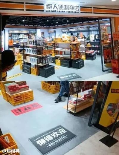 这是一张原始拍摄的静态图，呈现了一家以“懒人”为主题的线下便利商店。店铺入口上方的招牌清晰标注“懒人便利商店”，门口的地垫印有“懒得欢迎”的字样，还有一块红色标识写着“注注意”，这些文字都贴合店铺的“懒人”趣味定位，营造出诙谐放松的氛围。店内空间陈列着各类商品，使用黑色储物箱和黄色塑料筐作为陈列容器，风格随性。图中可见一个人的下半身，正处于店内区域，似乎在行走活动。画面左下角带有“小鸡词典”的水印，表明图片的传播平台。