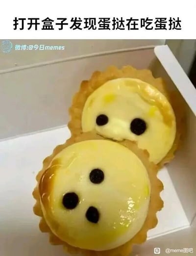 这是一张创意搞笑的静态单图，展示了装在白色盒子里的两个蛋挞。创作者在蛋挞的蛋液部分用黑点画出拟人化的五官，上方的蛋挞有两个黑点作为眼睛，下方的蛋挞有三个黑点组成眼睛和嘴巴，再将两个蛋挞上下叠放，让上方的蛋挞看起来像是趴在下方的蛋挞上，配合图片顶部的文字“打开盒子发现蛋挞在吃蛋挞”，制造出有趣的拟人化视觉错觉，把普通的美食赋予了互动感，显得十分可爱搞笑，属于利用日常美食进行创意加工的梗图。