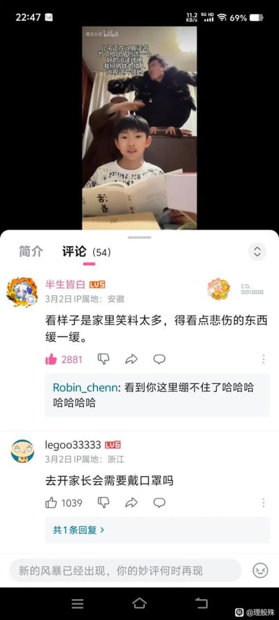 图片为手机屏幕截图，显示一段视频及下方评论区。视频中，一名儿童坐在桌前阅读一本名为《苦素》的书籍，表情认真；其身后有一名成人俯身，做出类似轻抚儿童头部的搞怪手势。视频上方配有文字：“儿童在运动讲述 万物的道理都在一个 故事的背后 等待被发现”。评论区共54条评论，置顶评论来自用户“半生皆白”（安徽IP）：“看样子是家里笑料太多，得看点悲伤的东西缓一缓。”获2881点赞；另有用户“legoo33333”（浙江IP）评论：“去开家长会需要戴口罩吗”获1039点赞，引发互动。整体场景充满家庭生活气息与幽默调侃氛围。