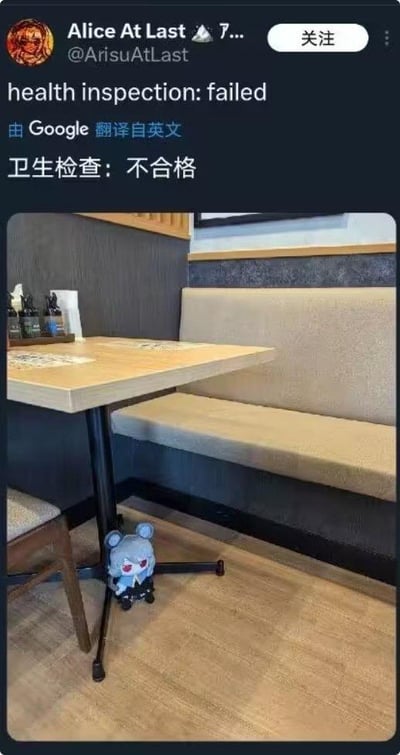 一张社交媒体截图梗图，内容是Twitter用户Alice At Last发布的餐厅照片。照片中展示了一个看起来干净整洁的餐厅座位区，桌子上摆放着餐具和调味品，但桌子下方却有一个蓝色的小毛绒玩具。配文写着"health inspection: failed"（卫生检查：不合格），暗示这个毛绒玩具是导致卫生检查失败的原因，用反差制造幽默效果。